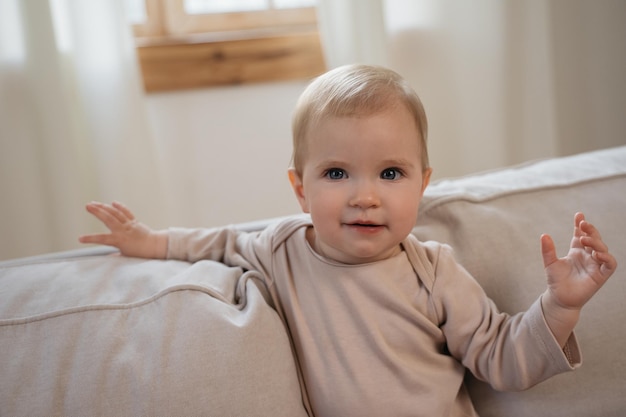 portrait of cute baby girl with beautiful eyes waving hand looking at camera sitting at home