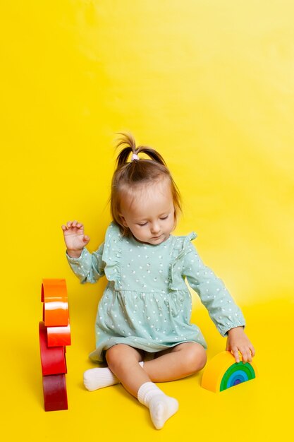 虹のデザイナーと遊んで、黄色の背景に青い目をしたかわいい女の赤ちゃんの肖像画。教育ゲームやおもちゃ。子供に教える。色。テキストの場所。高品質の写真