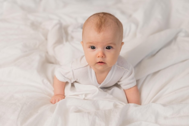 portrait of a cute baby in a white bodysuit on a bed at home with white linens. Newborn baby at home