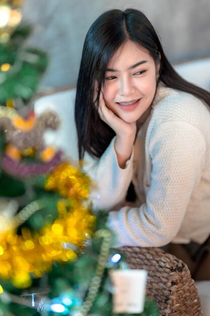 Portrait Cute beautiful positive smile young asian woman decorating to a Christmas tree at home in the living room indoors Decoration During Christmas xmas and New Year holidays