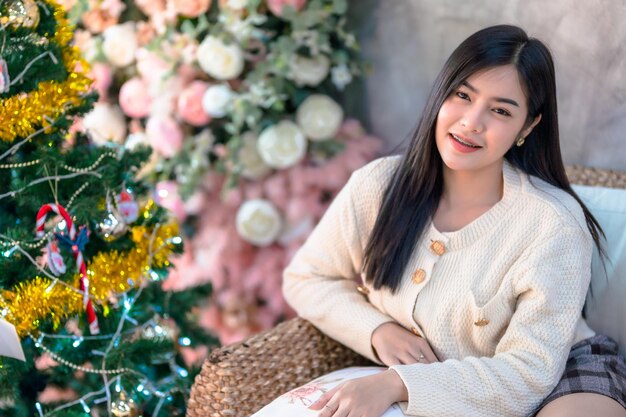 Portrait Cute beautiful positive smile young asian woman decorating to a Christmas tree at home in the living room indoors Decoration During Christmas xmas and New Year holidays