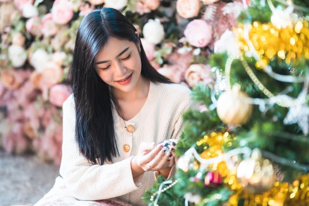 Ritratto carino bel sorriso positivo giovane donna asiatica che decora un albero di natale a casa nel soggiorno al chiuso decorazione durante le vacanze di natale e capodanno