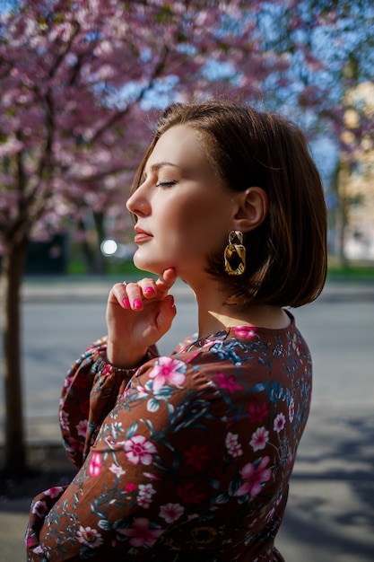 Portrait of a cute and beautiful woman girl in a dress in the garden in the middle of blooming sakura. spring and sun time. Blurred background and selected focus.