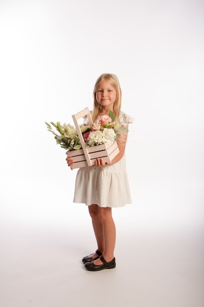 Ritratto di ragazza bionda carina in abito bianco con cesto di fiori in legno