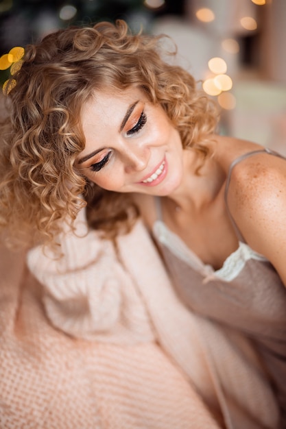 Портрет милой блондинки с вьющимися волосами в уютной домашней одежде