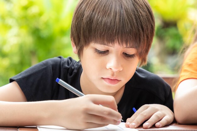 Портрет милого мальчика, рисующего и делающего домашнее задание в саду дома