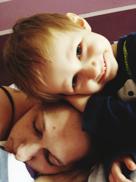 Photo portrait of cute boy lying on mother sleeping at home