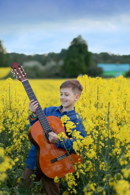 Ritratto di ragazzo carino che suona una chitarra nel campo giallo estivo. bambino che si diverte a immaginarsi una superstar.