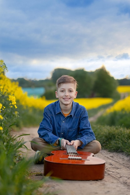 Ritratto di ragazzo carino che suona una chitarra nel campo giallo estivo