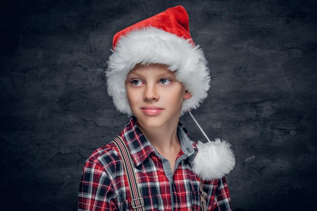 Portrait of cute boy in Santa's hat on grey background.