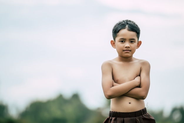 タイの伝統的なドレスに立って、胸に腕を組んで上半身裸のかわいい男の子の肖像画