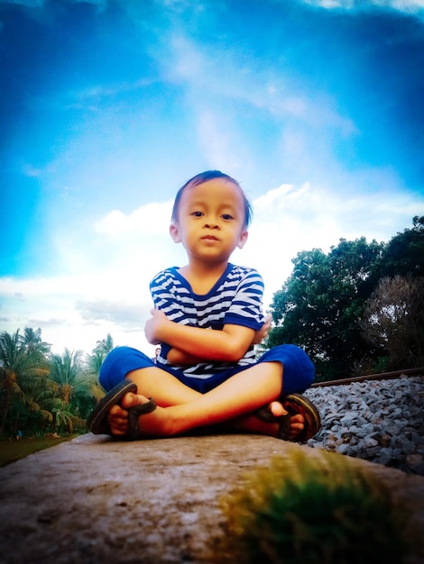 Portrait of cute boy sitting against sky