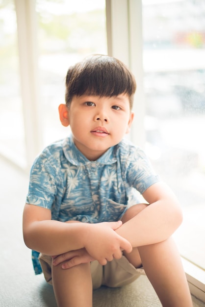 Photo portrait of cute boy sitting against window at home