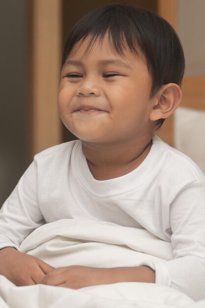 Photo portrait of cute boy sitting and smiling on bed at home