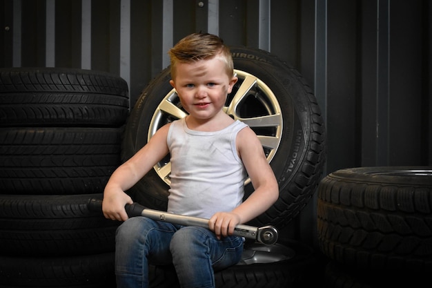 自動車修理店のタイヤに座っている可愛い男の子の肖像画