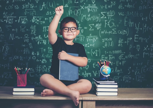 Portrait of cute boy wearing eyeglasses against blackboard in classroom