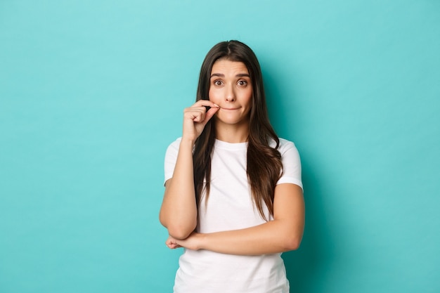 Portrait of cute brunette woman in white t-shirt making promise, seal lips, zipping mouth to hide