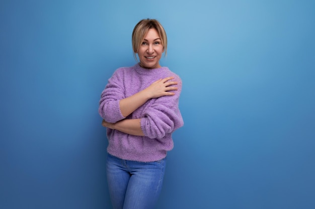 Portrait of a cute charming pleasant blond young woman in a purple sweater on a blue background with