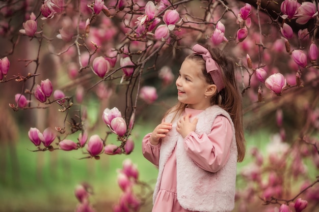 Portrait of a cute cheerful girl near a magnolia flower tree