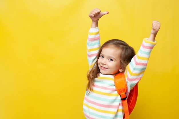 Portrait of a cute cheerfully laughing girl with a backpack Back to school Thumbs up