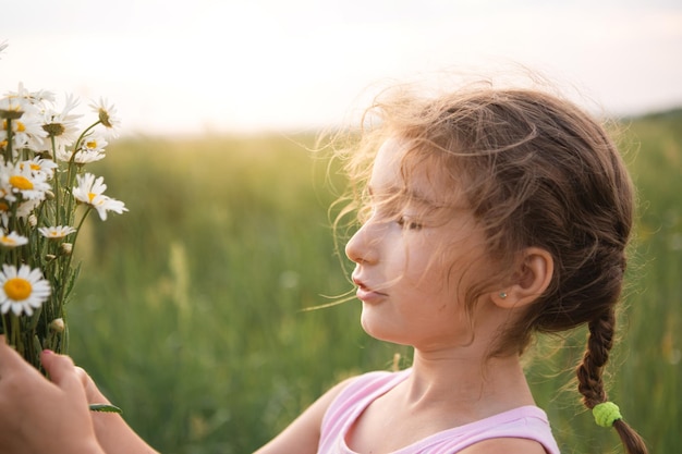 Portrait cute child girl with a bouquet of chamomile in summer\
on a green natural background happy child hidden face no face\
covered with flowers copy space authenticity rural life\
ecofriendly