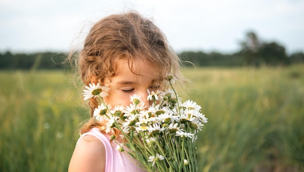Portrait cute child girl with a bouquet of chamomile in summer\
on a green natural background happy child hidden face no face\
covered with flowers copy space authenticity rural life\
ecofriendly