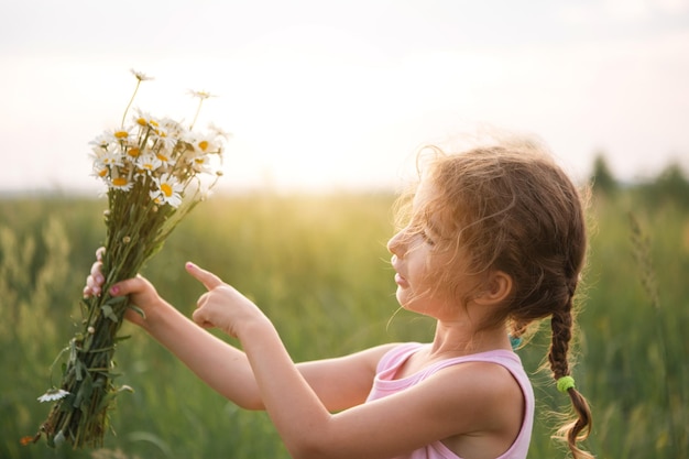 Portrait cute child girl with a bouquet of chamomile in summer on a green natural background Happy child hidden face no face covered with flowers Copy space Authenticity rural life ecofriendly