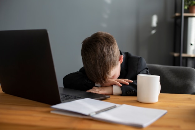 Photo portrait of cute child with suit sitting at the desk with laptop and mug