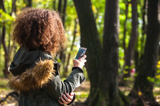 秋の森のスマートフォンでかわいい巻き毛の十代の少女の肖像画