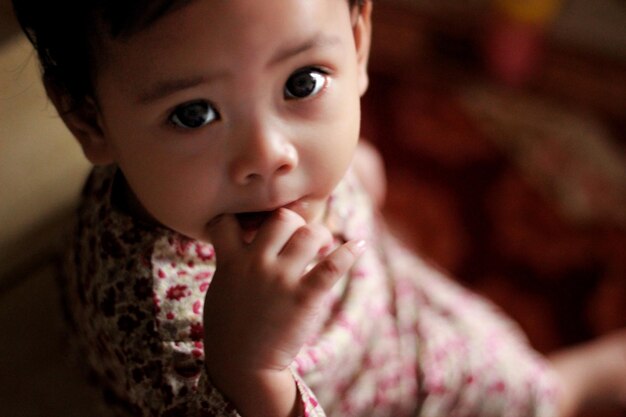 Photo portrait of cute girl biting finger while sitting at home