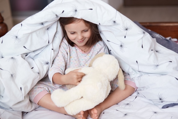 Portrait of cute girl and dog toy under blanket