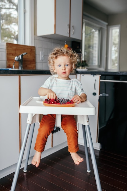 Photo portrait of cute girl eating berries at home