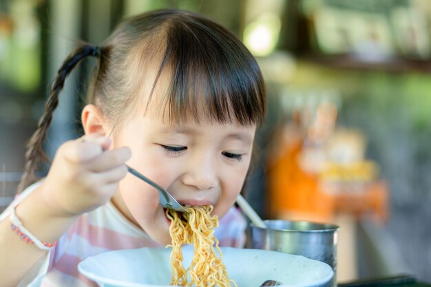 Photo portrait of cute girl eating noodles at restaurant