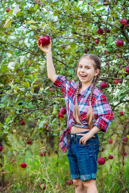 Portrait of a cute girl in a farm garden with a red apple Autumn harvest of apples