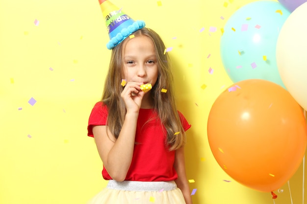 Portrait of cute girl in a festive cap and with balloons on colored background