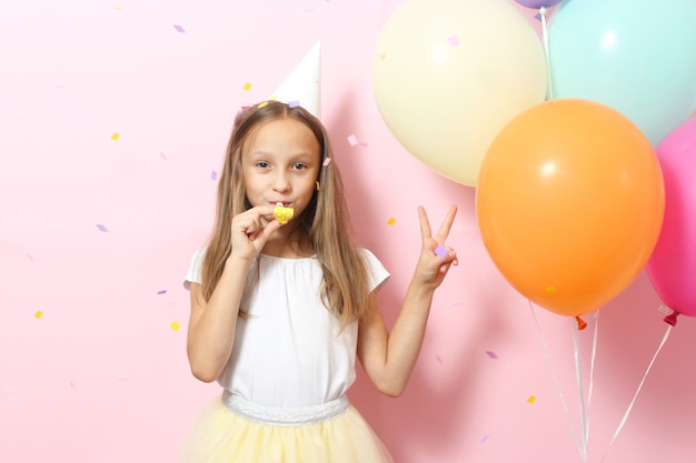 Portrait of cute girl in a festive cap and with balloons on colored background