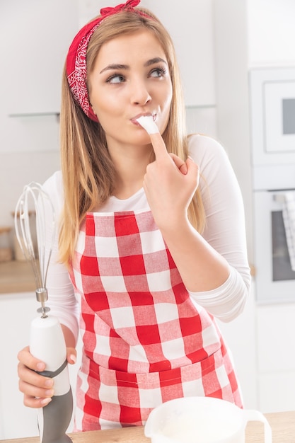 泡だて器の卵白をもう一方の手で泡だて器で指でなめるかわいい女の子の肖像画。