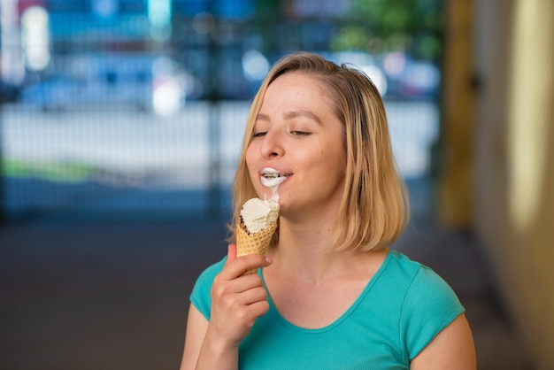 Portrait of a cute girl in a green dress is walking outside and eating dessert Beautiful blonde enjoying a cone with ice cream on a beautiful summer day Life is a pleasure