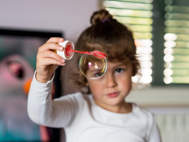 Portrait of cute girl holding bubble on wand at home