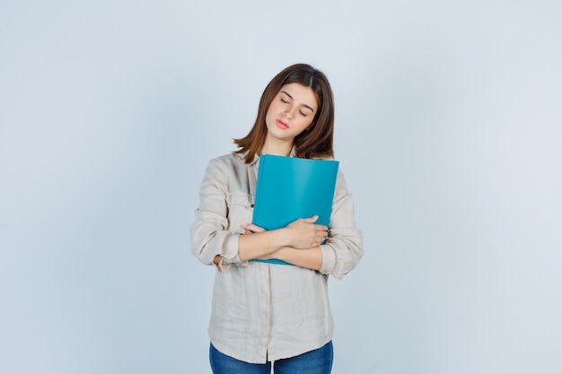 Portrait of cute Girl holding folder, shutting eyes in shirt and looking sleepy