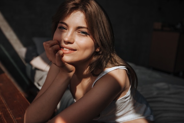 Portrait of a cute girl in the morning by the window on the bed in the sunlight