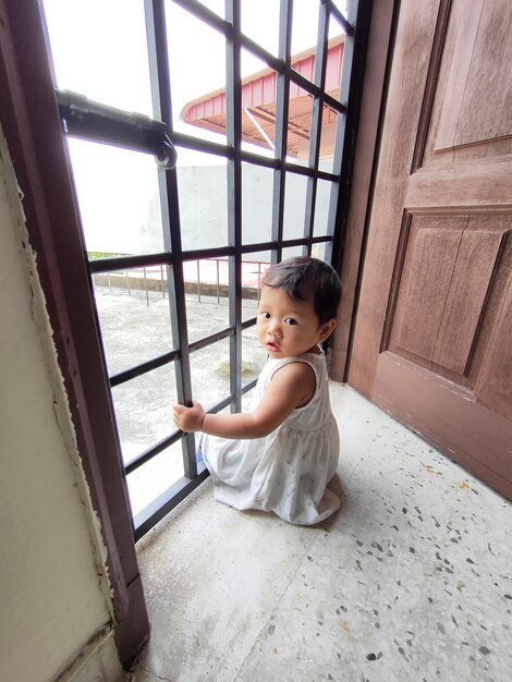 Photo portrait of cute girl sitting against window at home