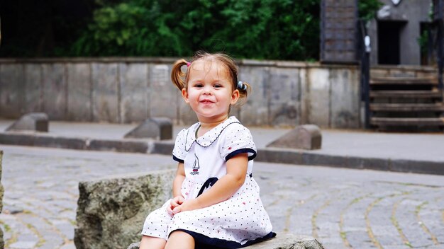 Photo portrait of cute girl sitting on footpath