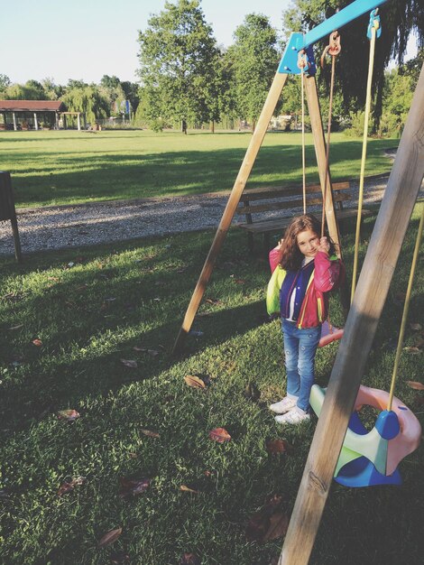 Foto ritratto di una ragazza carina in piedi vicino all'altalena al parco giochi