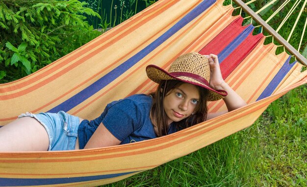 Portrait of a cute girl in a straw hat lying in a hammock