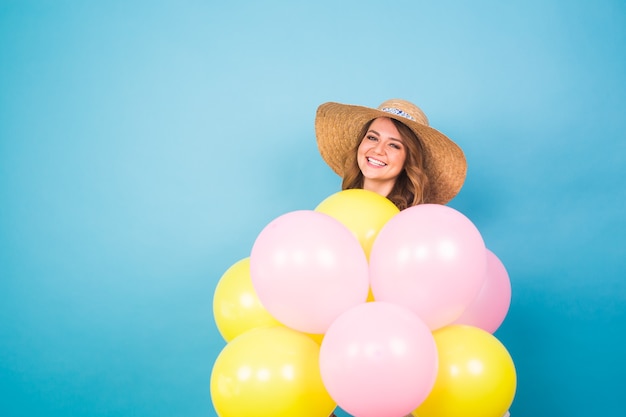 Portrait of cute girl in a studio smiling and playing with yellow and pink balloons, background with copyspace. Party, celebrate and people concept.