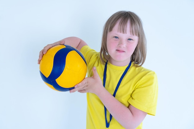 Portrait of a cute girl with blond hair with Down syndrome  holds a yellowblue volleyball ball