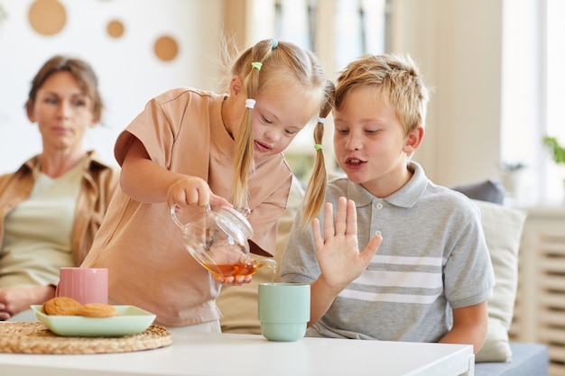 自宅で家族との時間を楽しみながら、カップにお茶を注ぐダウン症のかわいい女の子の肖像画、コピースペース