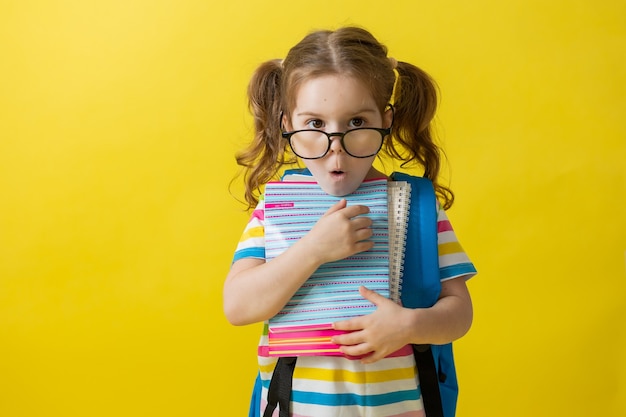 Portrait of a cute girl with glasses in a striped Tshirt with notebooks and textbooks in her hands