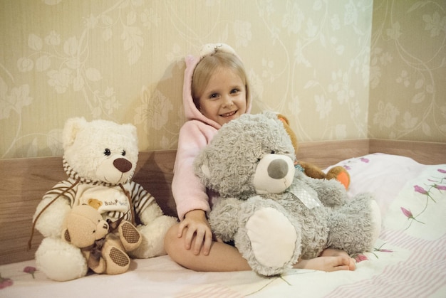 Photo portrait of cute girl with various teddy bears on bed at home